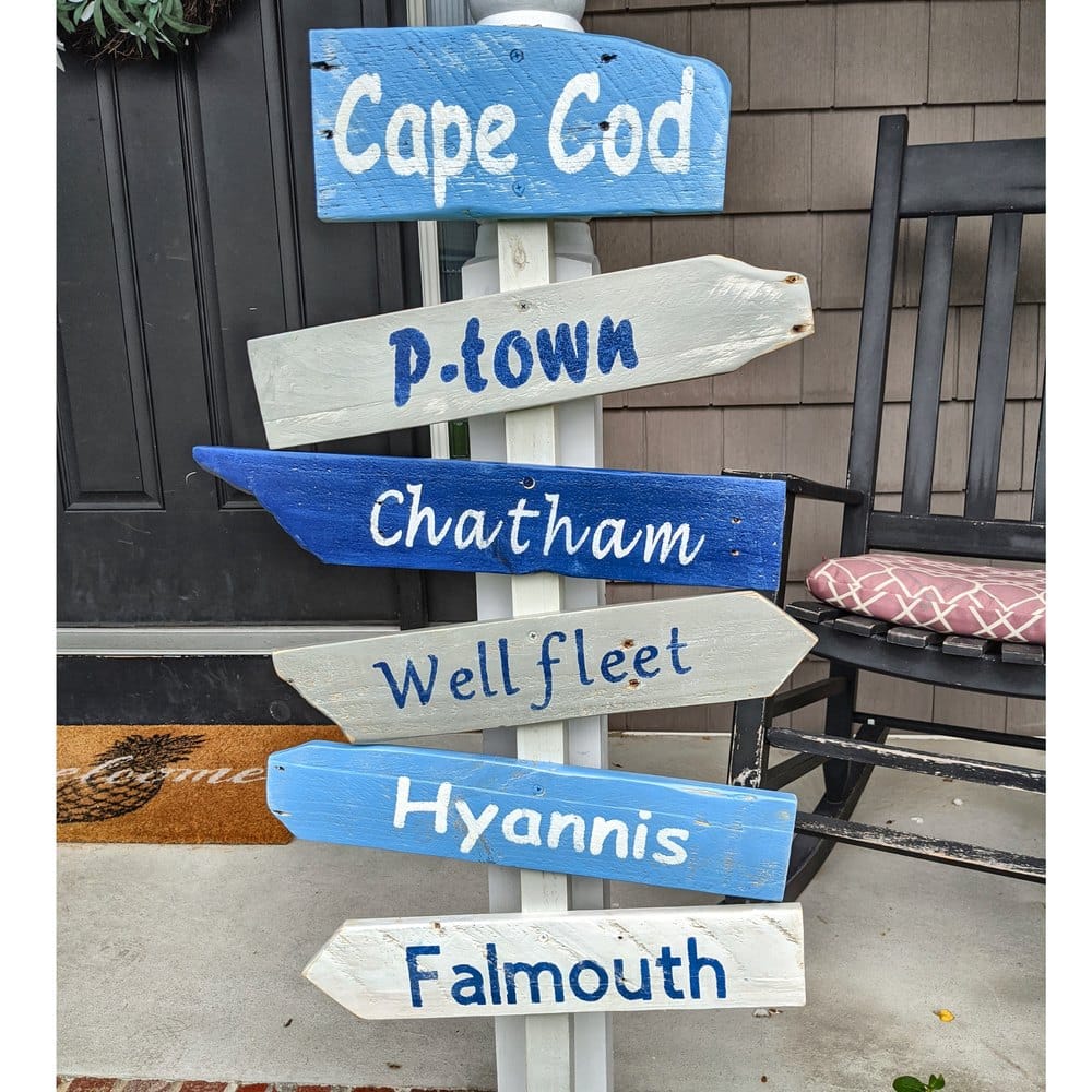 A hand-painted Cape Cod directional sign beside a shingled front door