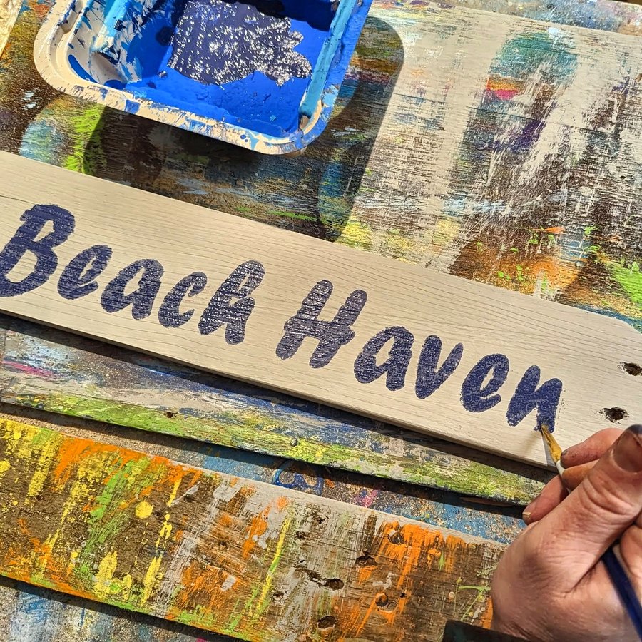 A hand painting lettering onto a reclaimed wood sign