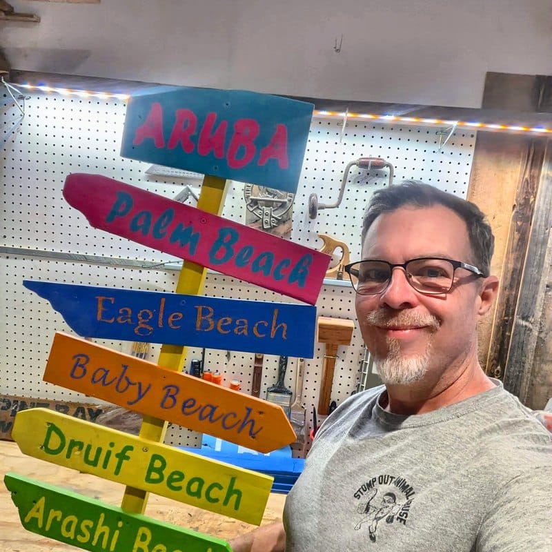 Tim in his woodshop holding a finished Aruba directional sign